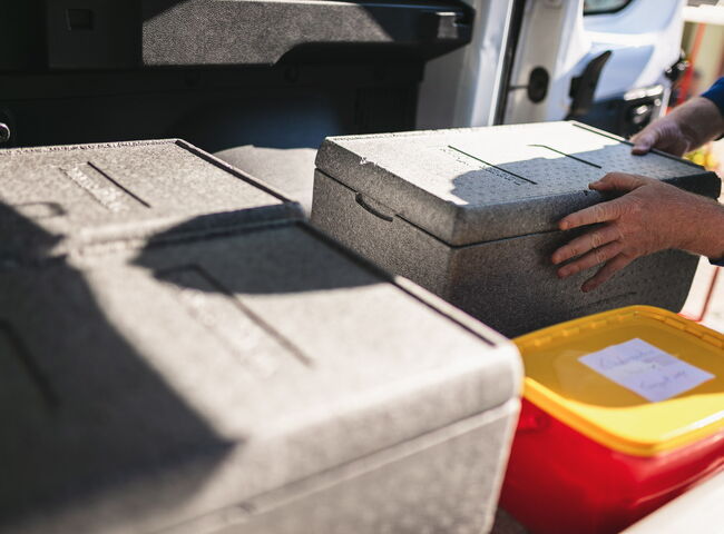 Eine Mitarbeiterin lädt Transportboxen aus dem Firmenfahrzeug