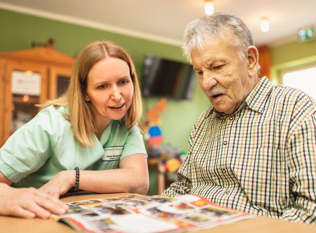 Eine Mitarbeiterin liest zusammen mit einem Bewohner eine Zeitschrift