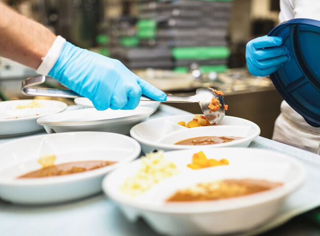 Gemüse wird mit der Kelle in die Teller portioniert