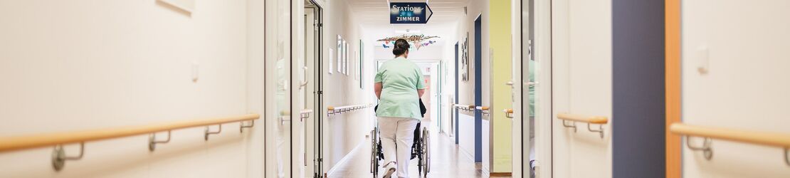 Pflegepersonal schiebt Rollstuhl