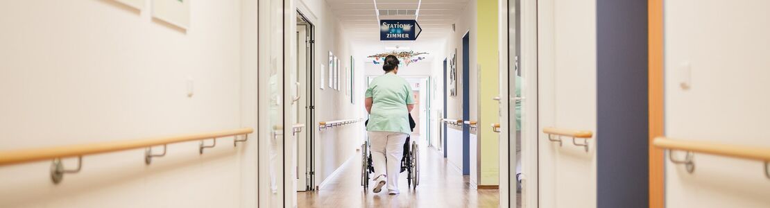 Pflegepersonal schiebt Rollstuhl