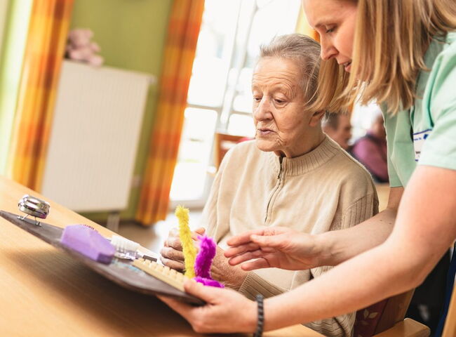 Eine Mitarbeiterin übt mit einer Bewohnerin an einem Motorikbrett