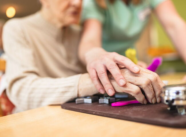 Die Hand einer Bewohnerin wird auf einem Motorikbrett geführt