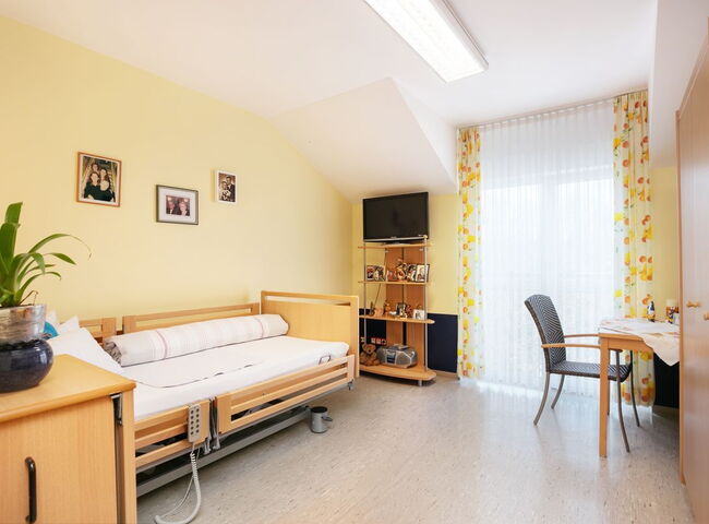 Blick in ein bewohntes Zimmer mit Pflegebett, Tisch und Stuhl